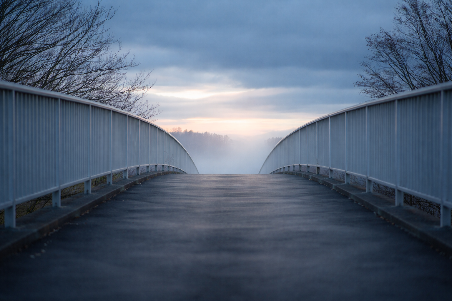 A quiet pedestrian bridge leading into mist and open horizon, symbolizing transition, uncertainty, and moving toward an unknown future.